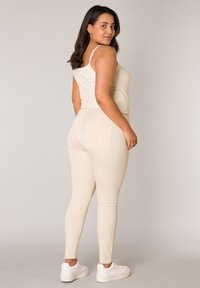 Beige tanktop met dunne bandjes, gecombineerd met bijpassende skinny pants met een achterzak, afgewerkt met witte sneakers. Soepele textuur.