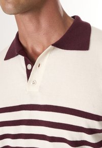 Kreemikarva polo särk maroon ribaadega, lühikese kaelusega ja kahe nupuga nööpide rida. Pehme kudumisstruktuur ja tavalise lõikega.