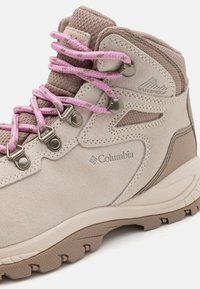 Botte de randonnée imperméable beige en matériau suédé, avec des lacets roses, des œillets en métal et des accents texturés sur la semelle pour une meilleure adhérence.