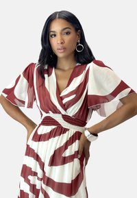 Robe fluide blanche avec un motif abstrait bordeaux; elle présente un décolleté en V profond, de courtes manches volantées et une taille smockée. Texture lisse.
