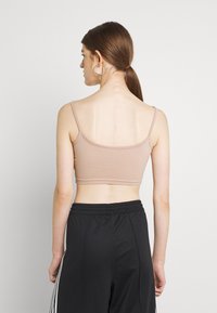 Svijetlosmeđa kratka majica bez rukava s tankim naramenicama, izrađena od rastezljivog materijala, u kombinaciji s crnim sportskim hlačama s bijelim bočnim prugama.