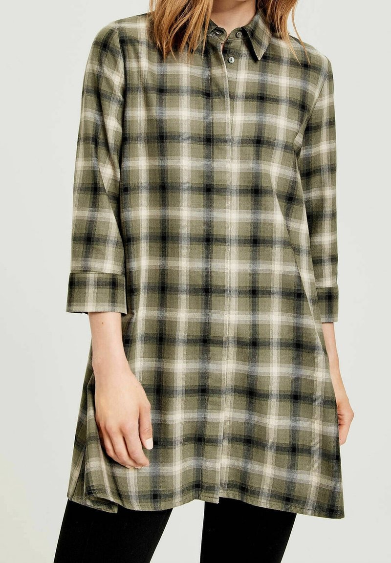Túnica de cuadros verde y crema con cuello de botón, mangas tres cuartos y un corte holgado. Presenta un dobladillo recto y una textura de tela suave.