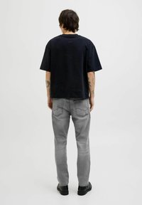 Svart kortärmad t-shirt med en avslappnad passform, parat med ljusgrå jeans med bakfickor. Bärs med svarta skor.