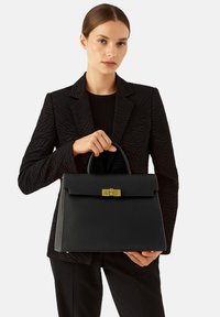 Borsa a mano in pelle nera con forma strutturata, manico superiore e dettagli metallici dorati. L'esterno presenta una superficie testurizzata e una chiusura a pattina.
