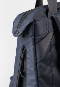 Dunkelblauer Rucksack aus Stoffmaterial, mit Reißverschluss und einem oberen Klappdeckel mit Druckknopf. Enthält verstärkte Nähte und verstellbare Träger.