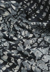 Schwarz-weißer, gemusterter Stoff, der drapiert ist und eine strukturierte Oberfläche mit abstrakten Formen sowie ein sanft fließendes Erscheinungsbild aufweist.