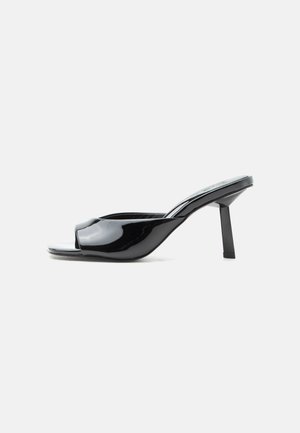 Mule ouverte à orteils noirs brillants avec un talon carré mi-haut et une bride incurvée sur le devant, sur fond blanc.