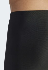 Tissu noir extensible avec une texture lisse, formant un vêtement de bas ajusté avec un design de ceinture simple et épuré.