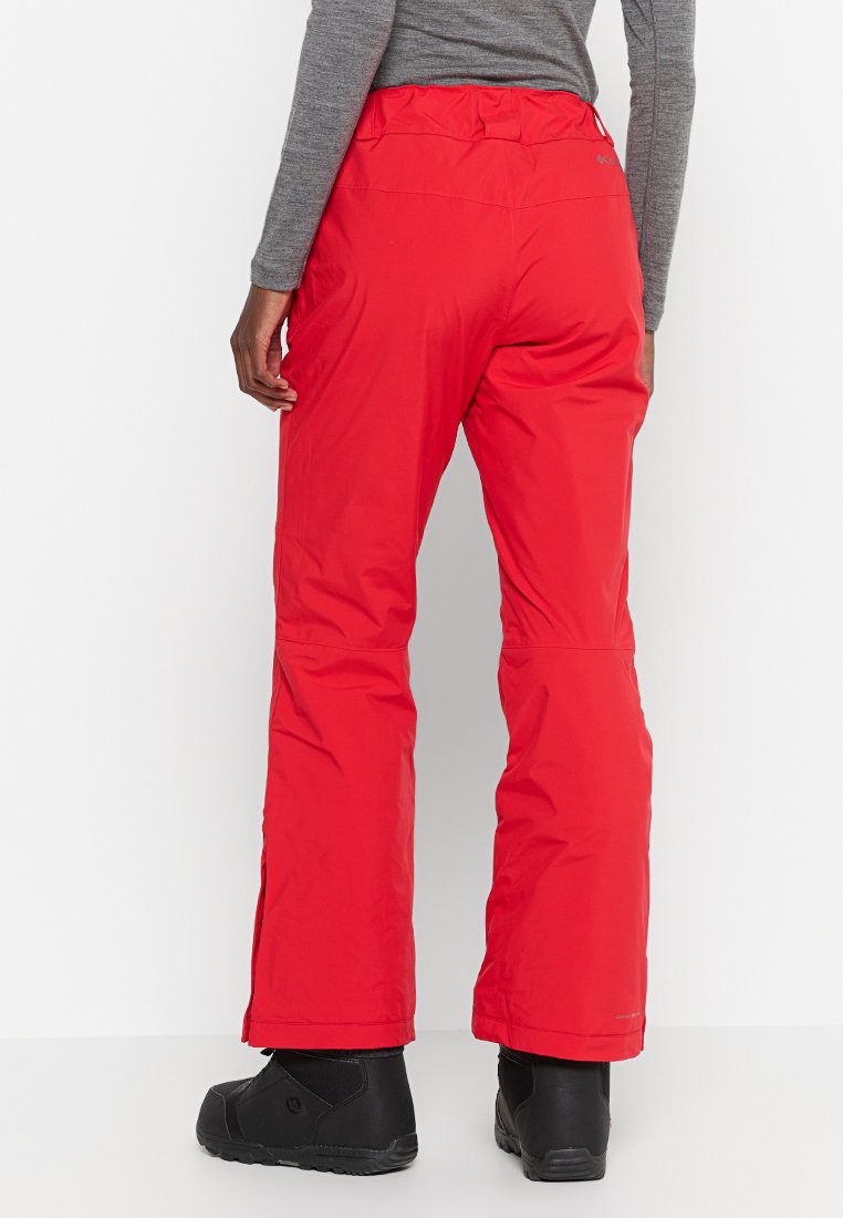 Pantaloni da neve impermeabili rossi con design a gamba dritta, cintura elastica e dettagli con zip, abbinati a stivali invernali neri.