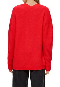 Roter gestrickter Pullover mit V-Ausschnitt und überschnittenen Schultern. Hat eine gerippte Textur und einen lockeren Schnitt. Der Saum ist hinten abgerundet.