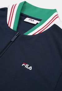 Marineblauwe zip-up jack met groene kraag en gestreepte accenten in rood en wit. Beschikt over een geborduurd Fila-logo op de linkerbovenborst. Zachte stof textuur.