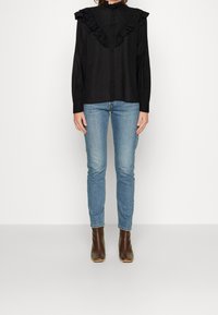 Blusa nera a maniche lunghe con dettagli di colletto arruffato, abbinata a jeans skinny blu chiaro e stivaletti marroni.