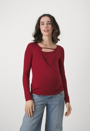 Rød bluse med lange ærmer og crossover-design, med en udskæring i halsen og rynkede sider. Sammen med lys blå brede jeans.