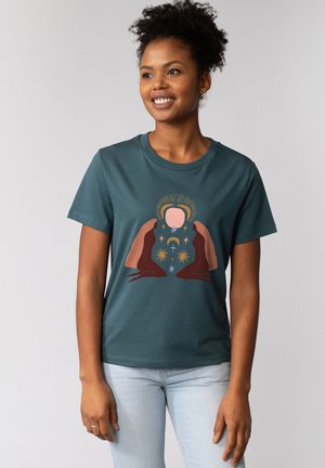 Teal katoen T-shirt met een grafisch ontwerp van twee figuren met lang haar, sterren en een zonmotief, tegen een neutrale achtergrond.