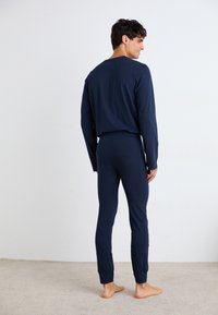 Marineblaues Langarmoberteil und passende, eng anliegende Hose aus weichem Stoff. Mit Rundhalsausschnitt, engen Bündchen und einem einfachen, klaren Design.