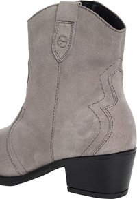 Botín de ante gris con detalles de costura curva. Presenta una punta redonda y un tacón corto y apilado en negro. Lleva una lengüeta en la parte superior.