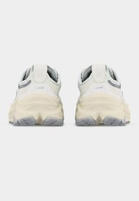 Ζευγάρι λευκών και μπεζ αθλητικών παπουτσιών με χοντρές σόλες, που φαίνονται από πίσω, σε απλό ανοιχτόχρωμο φόντο.