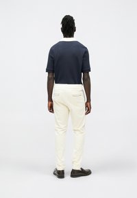 Granatowy dzianinowy polo z białym kołnierzykiem, w połączeniu z kremowymi spodniami z bocznymi kieszeniami, noszone z brązowymi mokasynami. Widok od tyłu.