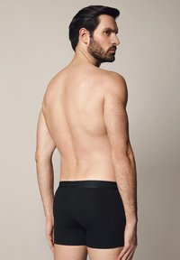 Czarne bokserki o gładkiej fakturze, z miękkim pasem biodrowym z logo. Model widziany od tyłu na neutralnym tle.