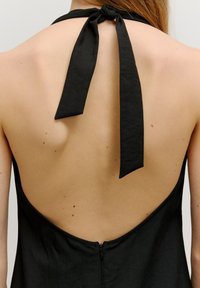 Schwarzes Neckholder-Kleid mit einem tiefen Rückendesign, gebundenen Nackenriemen und einem verdeckten Reißverschluss im unteren Rückenbereich. Glatte Textur des Stoffes.
