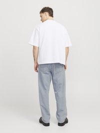 Camiseta de algodón blanca con corte relajado, mangas cortas y dobladillo recto, combinada con unos vaqueros de corte relajado en azul claro y zapatos negros.