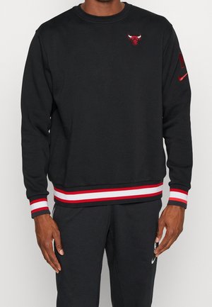 Mand iført sort Chicago Bulls sweatshirt med røde og hvide stribede ærmekanter og kant, kombineret med sorte bukser med hvid Nike-logo.
