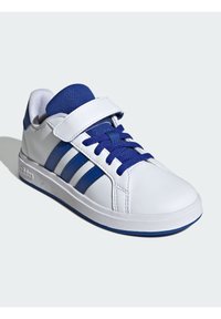 Basket blanche avec des accents bleus et trois bandes diagonales. Dispose d'une semelle en caoutchouc plate, d'une languette en tissu texturé et d'une sangle à scratch.