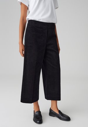 Pantaloni a gamba larga in velluto a coste neri con una superficie testurizzata e vita aderente. Abbinati a mocassini neri e una t-shirt bianca semplice.