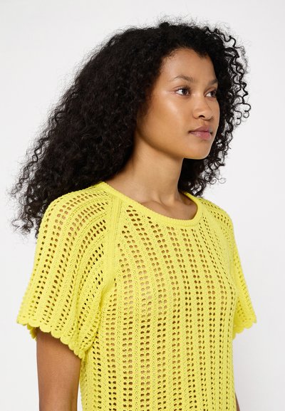 Top amarillo de punto, de manga corta, con un patrón de tejido abierto y bordes con forma de concha, que presenta un cuello redondo y una textura ligera.