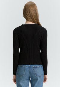 Schwarzer gerippter Strickpullover mit langen Ärmeln und rundem Ausschnitt, kombiniert mit hellblauen hochgeschnittenen Jeans mit Gesäßtaschen.