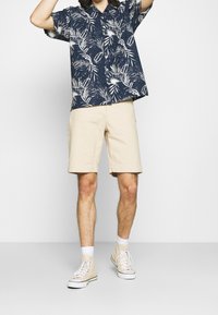 Short-sleeve navy shirt with white palm leaf pattern, paired with beige shorts, and light-colored high-top sneakers featuring white laces.
