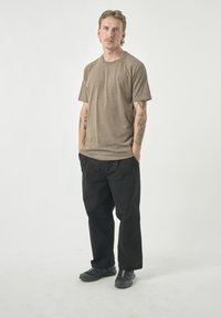 Braunes T-Shirt mit kurzen Ärmeln kombiniert mit lockeren schwarzen Hosen. Das Outfit wird durch schwarze Schuhe mit kleinen Farbakzenten ergänzt.