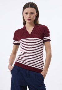 Pull polo tricoté en bordeaux et blanc, avec un col en V, une texture côtelée et des rayures horizontales. Manches courtes avec des poignets contrastés.