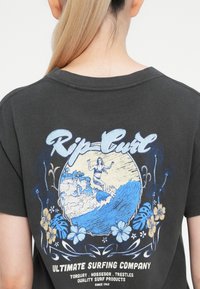 Temno siva bombažna majica z modro-belo grafično zasnovo, ki prikazuje surferko sceno s cvetličnimi poudarki in besedilom "Rip Curl."