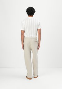 Witte, ribbelige trui met korte mouwen, gecombineerd met beige broek met elastische tailleband en een achterzak. Glad weefsel en rechte pasvorm.