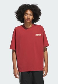 Červené bavlněné tričko s volným střihem, krátkými rukávy a kulatým výstřihem. Na hrudi má bílé logo "adidas BASKETBALL".