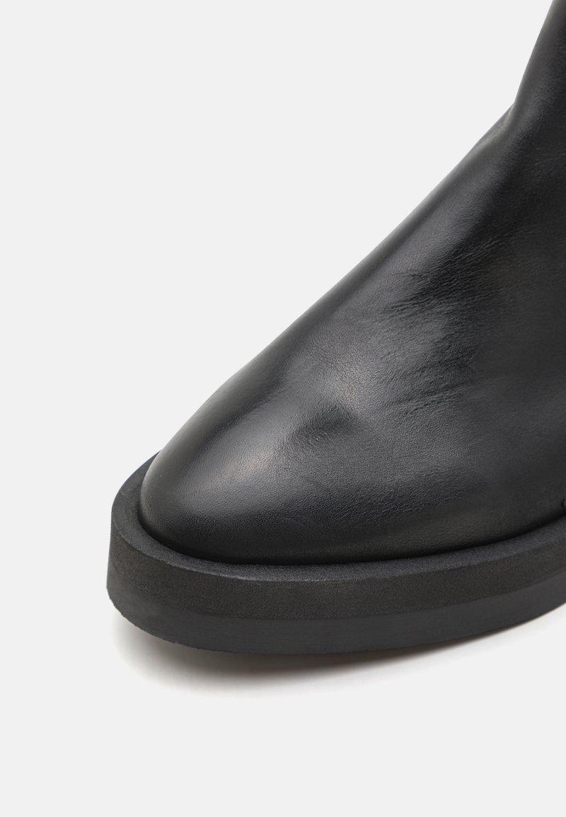 Schwarze Leder-Ankle-Boots mit spitzer Zehenpartie, ausgestattet mit einer dicken schwarzen Gummisohle und glatter Textur.