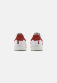Białe sneakersy z czerwonymi skórzanymi akcentami na pięcie, górna część z gładkiej skóry, okrągły czubek i teksturowana podeszwa z gumy. Minimalistyczny design z detalem logo.