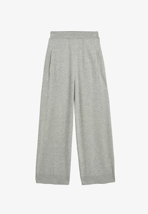 Tułów i biodra kobiety w jasnoszarej dzianinowej spódnicy i krótkim swetrze, ręka umieszczona w kieszeni spódnicy na neutralnym tle.