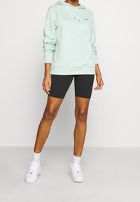 Mintgrön hoodie med en framficka, guld Nike-logotyp. Matchas med svarta cykelshorts och vita sneakers, med vita strumpor.