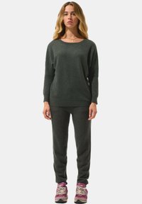 Dunkelgrüner Pullover und passende Hose aus weichem Stoff, mit entspannter Passform und Rundhalsausschnitt, kombiniert mit mehrfarbigen Turnschuhen.