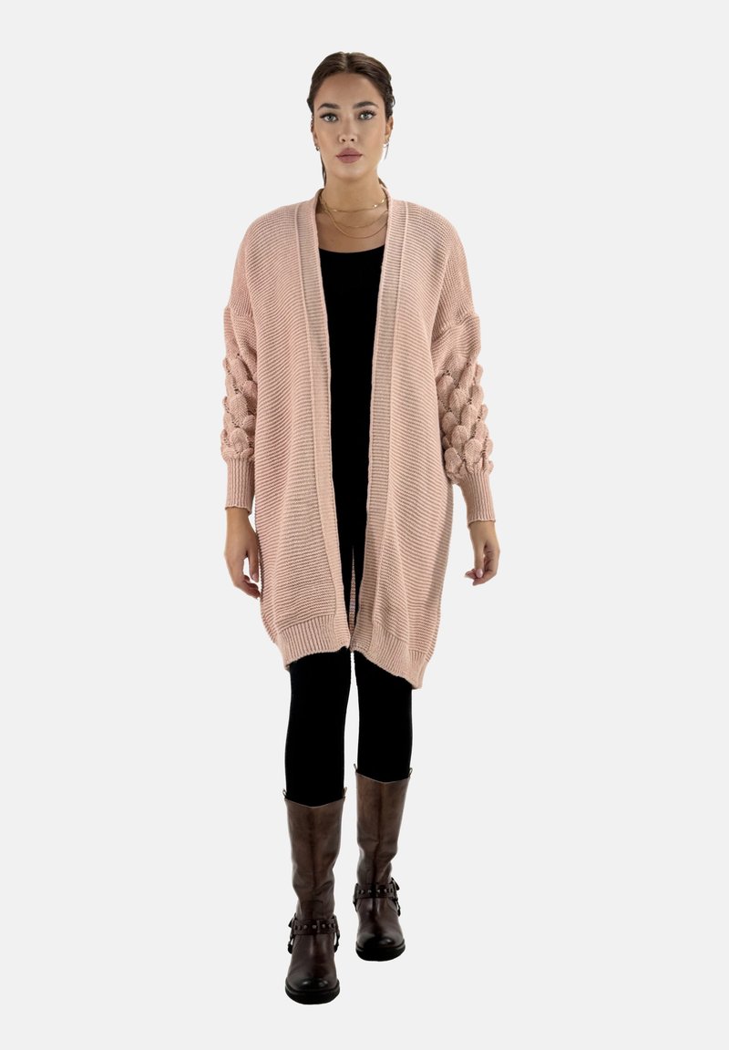 Lång, öppen cardigan i mjuk rosa stickning, med texturerade puffärmar, använd över en svart topp ochleggings, tillsammans med bruna knähöga stövlar.