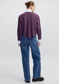 Camicia a quadri in blu navy e rosso con maniche lunghe e colletto bianco, abbinata a jeans blu a vita alta e stivali neri spessi.