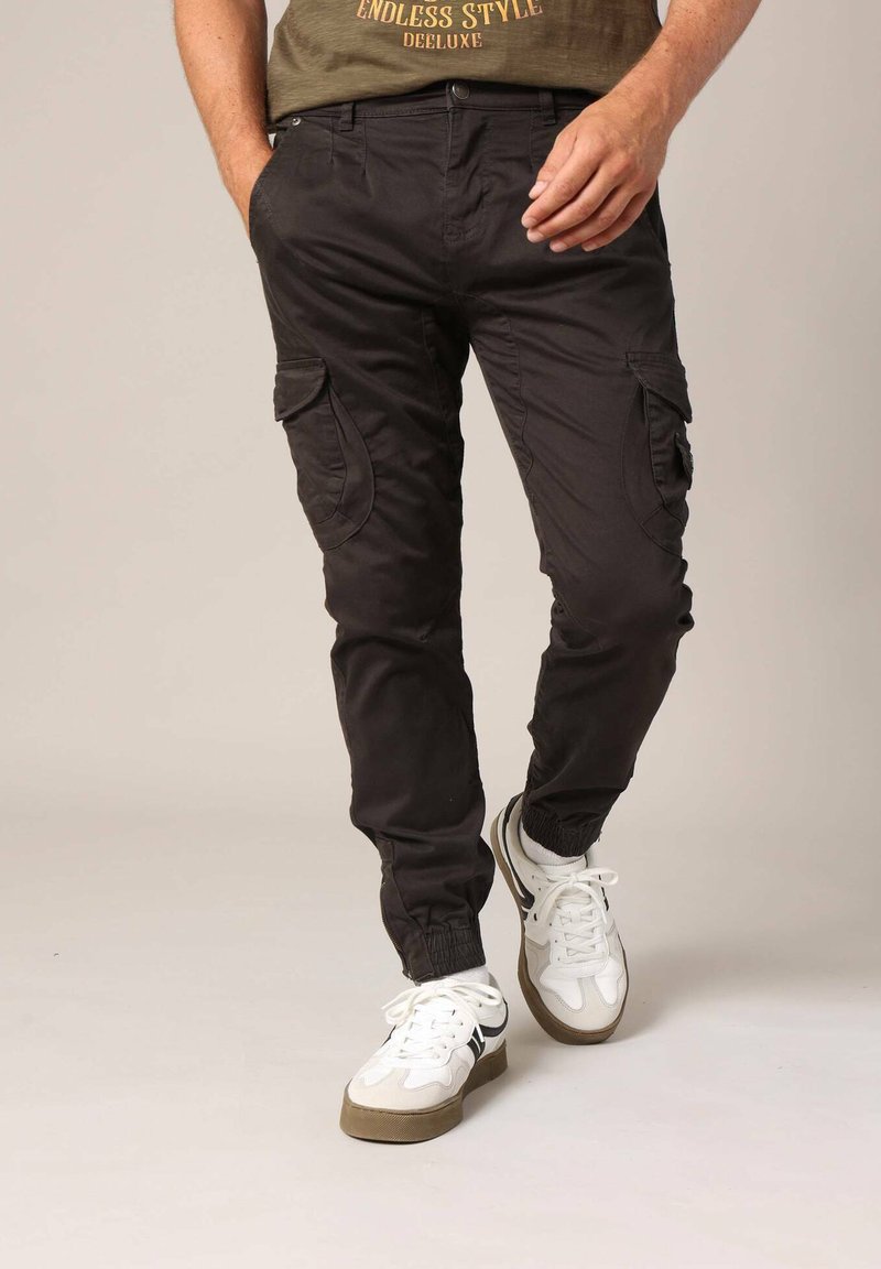 Zwarte cargobroek met elastische boorden en zijzakken, gecombineerd met witte sneakers. De broek heeft een gladde textuur en een aansluitend ontwerp.