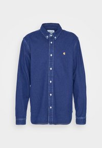 Camisa de mezclilla azul oscuro con botones, de manga larga, botones blancos y un pequeño logo amarillo en el lado izquierdo del pecho. Diseño sencillo y clásico.