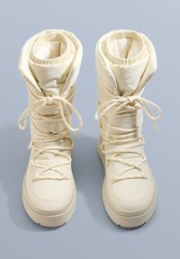 Beżowe ocieplone buty śniegowe z wysokim mankietem, ściąganym elastycznym wykończeniem oraz przodem z sznurówkami. Miękka tkanina o gładkiej fakturze i grubej podeszwie.