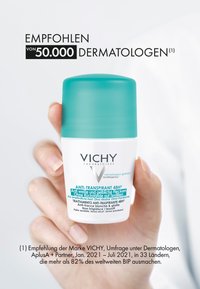 Vichy Anti-Transpirant 48h, cylindrical white bottle with teal cap, features white and teal text, held in a hand against a white background.