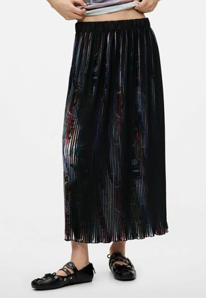 Mujer con falda midi plisada negra con sutiles reflejos de colores y zapatos planos negros con detalles recortados.