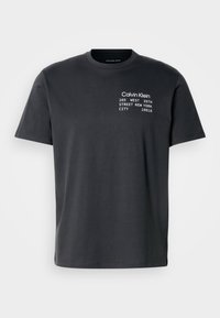 Σκούρο γκρι βαμβακερό T-shirt με κοντά μανίκια, που φέρει λευκό κείμενο που γράφει "Calvin Klein 205 WEST 39TH STREET NEW YORK CITY 10018."
