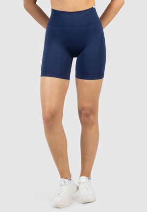 Pantalones cortos de compresión de talle alto en azul marino con diseño sin costuras. Textura suave y ajuste a la altura de la rodilla. Combinados con zapatillas deportivas blancas.